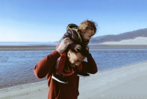 A father holding his child on his shoulders at the beach.
